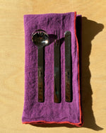 Set of silver cutlery on a purple cloth with a red border against a wood background