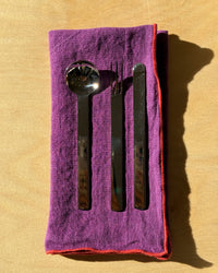 Set of silver cutlery on a purple cloth with a red border against a wood background
