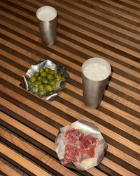 Two silver cups with a small dish of green grapes and another dish of red meat on a wooden surface.
