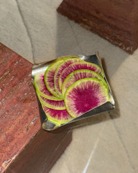 Sliced watermelon radishes on a metallic surface with a wooden background
