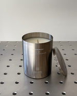 Silver candle container with a candle on a perforated metal surface