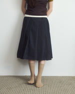 Person wearing a dark skirt with a white waistband against a plain background