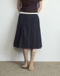 Person wearing a dark skirt with a white waistband against a plain background