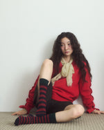 Person wearing a red sweater and black and red striped socks sitting on a white background