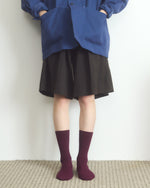 Person wearing a blue jacket, black skirt, and maroon socks on a plain background