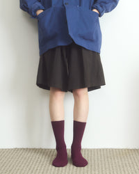 Person wearing a blue jacket, black skirt, and maroon socks on a plain background