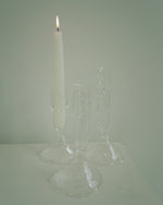 Clear glass candle holder with a lit white candle on a light gray background