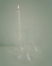 Clear glass candle holder with a lit white candle on a light gray background