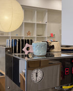 A countertop espresso machine in a kitchen setting, with ceramic mugs and a pink star-shaped object resting on its reflective stainless steel surface.