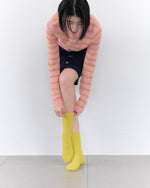 Person wearing a pink and yellow striped sweater and yellow socks on a white background