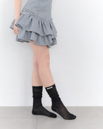 Person wearing a checkered skirt and black socks on a white background