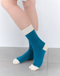 Teal socks with white accents worn by a person on a light gray floor.