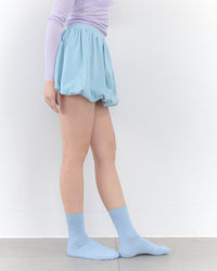 Person wearing a light blue skirt and socks on a white background