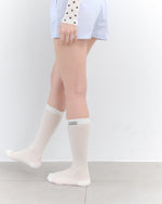 White knee-high socks worn by a person on a plain background