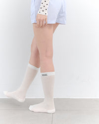 White knee-high socks worn by a person on a plain background