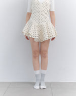 Person wearing a white polka dot dress with sheer white socks against a plain background