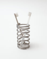 Metallic spring-like toothbrush holder with two toothbrushes on a white background