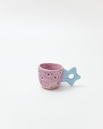 Pink ceramic cup with star patterns and a blue star-shaped handle on a white background