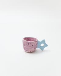 Pink ceramic cup with star patterns and a blue star-shaped handle on a white background