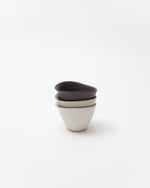Three ceramic cups, in white, beige, brown, stacked on a white background