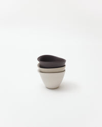 Three ceramic cups, in white, beige, brown, stacked on a white background