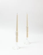 Two beige candles in clear candle holders on a white background