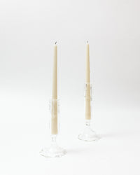 Two beige candles in clear candle holders on a white background