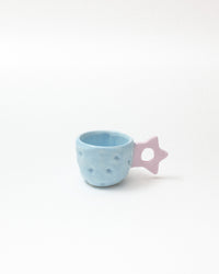 A small light blue textured ceramic cup with a pale purple star-shaped handle, set against a plain white background.