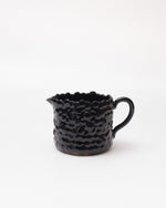 Black ceramic pitcher with textured surface on a white background