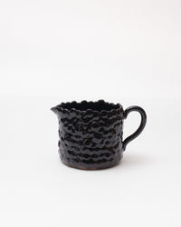 Black ceramic pitcher with textured surface on a white background