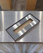 Metallic rectangular frame with cutout on a reflective surface