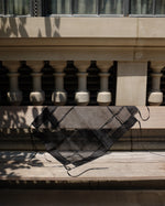 A black sheer mesh bandana with a diamond grid pattern draped over a wooden railing in front of a stone balustrade.