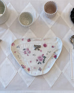 A white ceramic plate with a pink rose floral pattern and a small silver bow ornament in the center, displayed on a white diamond-patterned tablecloth.