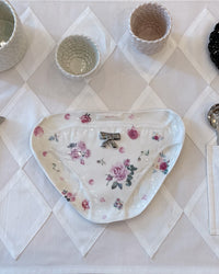 A white ceramic plate with a pink rose floral pattern and a small silver bow ornament in the center, displayed on a white diamond-patterned tablecloth.
