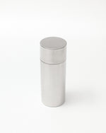 A minimalist, brushed stainless steel cylindrical container with a matching screw-top lid, shown on a seamless white background.