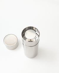 A stainless steel cylindrical container with a perforated top, shown open with its lid placed beside it on a clean white background.