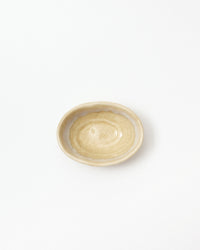 A small, shallow, oval ceramic dish with a rustic hand-painted finish in a light beige and cream glaze, shown from a top-down view on a solid white background.