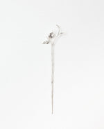 A delicate silver-toned metal flower stem pin with a small bud and leaf detail at the top, displayed vertically against a clean white background.