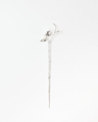 A delicate silver-toned metal flower stem pin with a small bud and leaf detail at the top, displayed vertically against a clean white background.