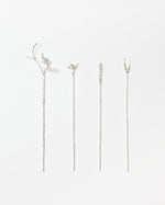 Four silver-toned metal pins with delicate botanical designs, including leaves, small branches, and a floral sprig, arranged vertically on a plain white background.