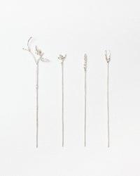 Four silver-toned metal pins with delicate botanical designs, including leaves, small branches, and a floral sprig, arranged vertically on a plain white background.