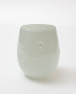 A translucent pale green glass tumbler with a rounded shape and small circular cutouts on the sides, photographed on a clean white background.