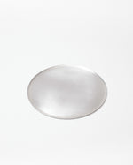 A single small circular silver-toned metal tray with a smooth, reflective surface, centered on a plain white background.