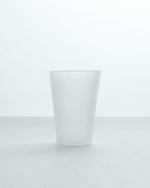 A frosted glass tumbler with a matte finish, standing upright on a light gray surface against a white background.