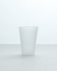A frosted glass tumbler with a matte finish, standing upright on a light gray surface against a white background.