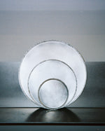 Three nested silver plates with textured edges, standing upright on a dark reflective surface against a gray background.