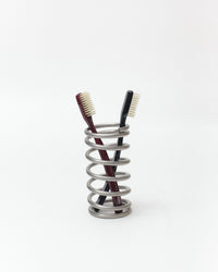 A silver metal spiral toothbrush holder containing two toothbrushes, one with a dark red handle and one with a black handle, set against a plain white background.