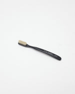 A single black toothbrush with beige bristles, featuring the brand name 'ACCA KAPPA' printed on the handle, set against a plain white background.