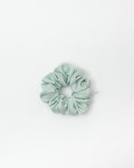 A melon green satin scrunchie centered on a clean white background.