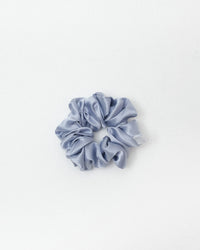 A single light blue-gray satin scrunchie centered on a clean white background.